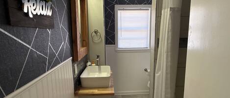 Un baño con un lavamanos blanco, un espejo y una ventana con persianas.