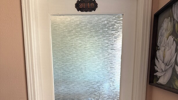 Una puerta blanca con un panel de vidrio esmerilado, un timbre negro y una placa con el número de la casa.