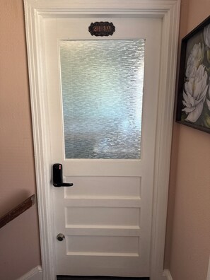 A white door with a frosted glass panel, a black doorbell, and a house number plaque.