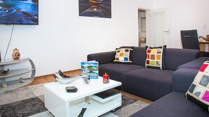 Una sala de estar con un televisor de pantalla plana grande, un sofá, una mesa de centro y una estantería.
