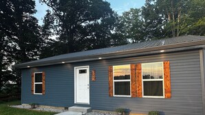 A modern two-story house with a grey exterior, a white front door, and wooden window shutters. - Charming 2-bedroom house in Devil's Elbow Osgood, IN (Osgood)