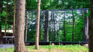 A forested area with a large black structure, possibly a viewing platform or observation deck, surrounded by trees and greenery. - MIRROR CABIN IN THE FOREST WITH HOT TUB (Windham)