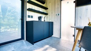 A modern kitchen with dark cabinetry, wooden shelves, and a large window. - MIRROR CABIN IN THE FOREST WITH HOT TUB (Windham)