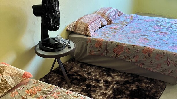 A bedroom with two beds, a standing fan, and a small table with a remote control.