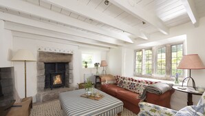 A cozy living room with a fireplace, a sofa, a coffee table, and a window with a view of greenery.
