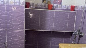 Een badkamer met paarse betegeling, een wit toilet, een houten wastafelmeubel met een wastafel en een douchehoek.