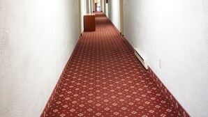 Un pasillo largo y estrecho de hotel con alfombra roja y paredes blancas.