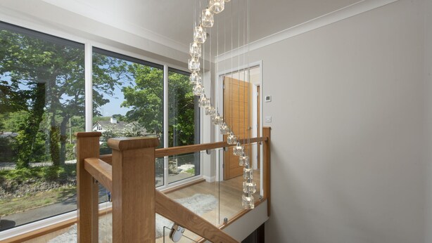 A modern interior with large windows, a wooden staircase, and a hanging light fixture. - Highfield Barton -  Hot tub, Free Wi-Fi (Reskadinnick)