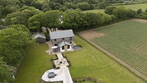 An aerial view of a house with a large lawn, a patio area, and a vineyard in the background. - Highfield Barton -  Hot tub, Free Wi-Fi (Reskadinnick)