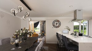 A modern kitchen with a large island, a dining area with a dark wood table and chairs, a decorative wall clock, and a view of the outdoors through large windows. - Highfield Barton -  Hot tub, Free Wi-Fi (Reskadinnick)