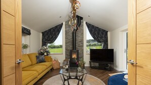 A modern living room with a yellow sofa, a glass coffee table, a fireplace, and a TV. - Highfield Barton -  Hot tub, Free Wi-Fi (Reskadinnick)