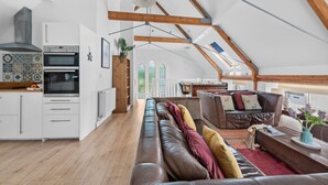 Um amplo loft com teto alto, vigas de madeira aparentes, cozinha equipada com eletrodomésticos modernos, área de estar aconchegante com sofás de couro e vista do céu através de um claraboia.