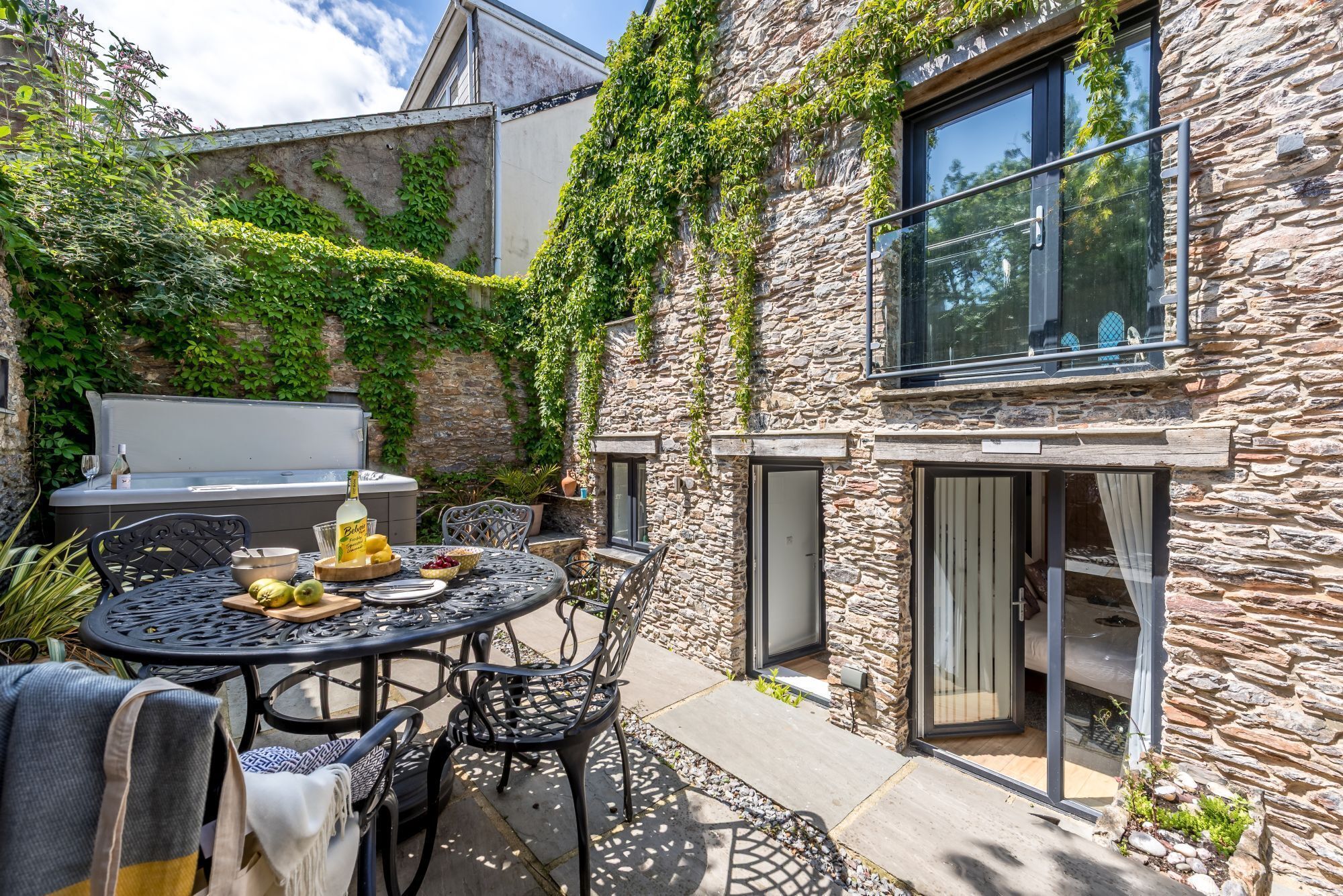 A stone house with a patio table and chairs, a grill, and a view of the surrounding greenery.
