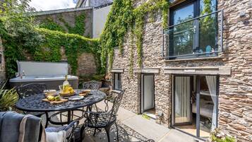 A stone house with a patio table and chairs, a grill, and a view of the surrounding greenery.