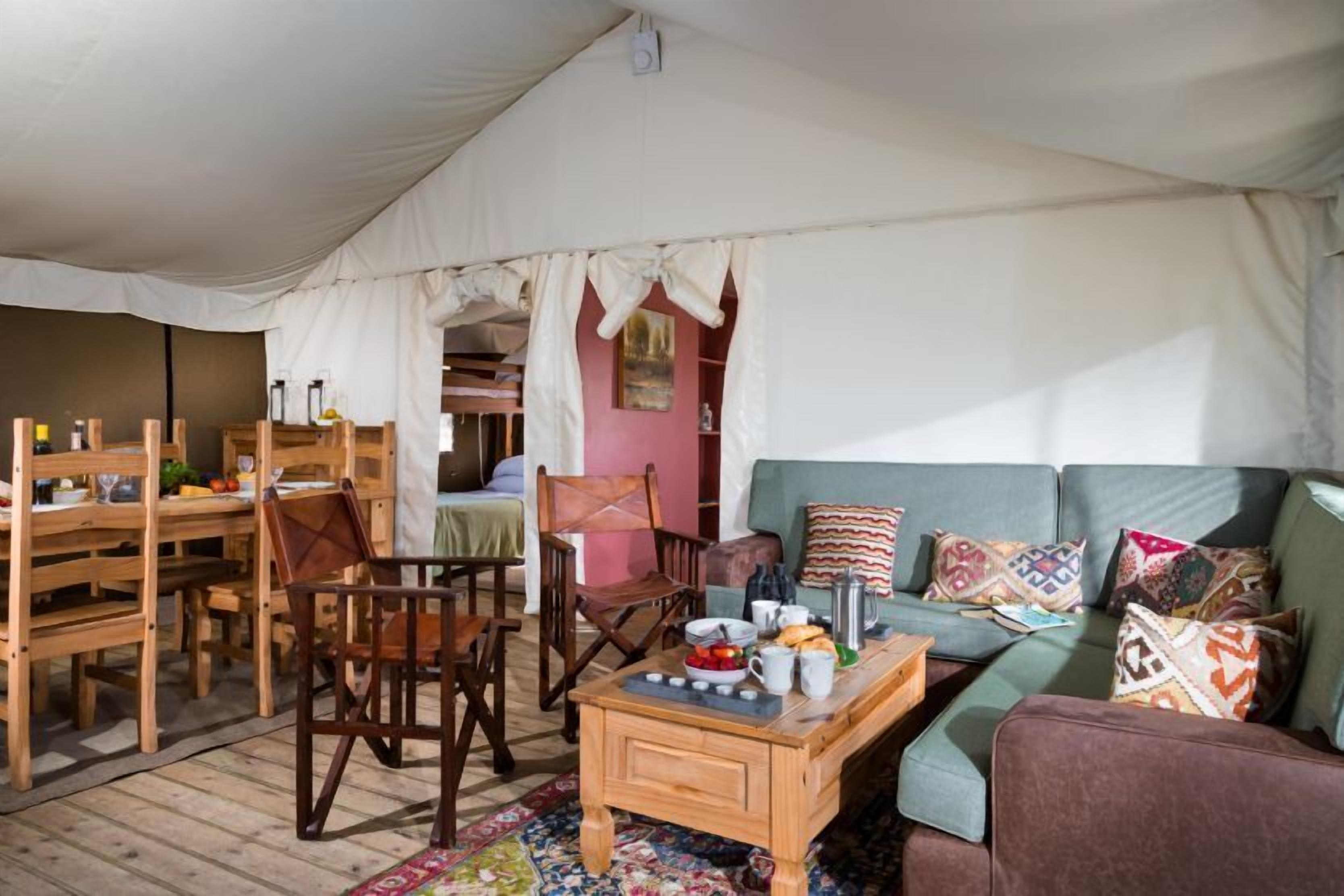 A tented accommodation with a dining area, a sofa, and a coffee table.