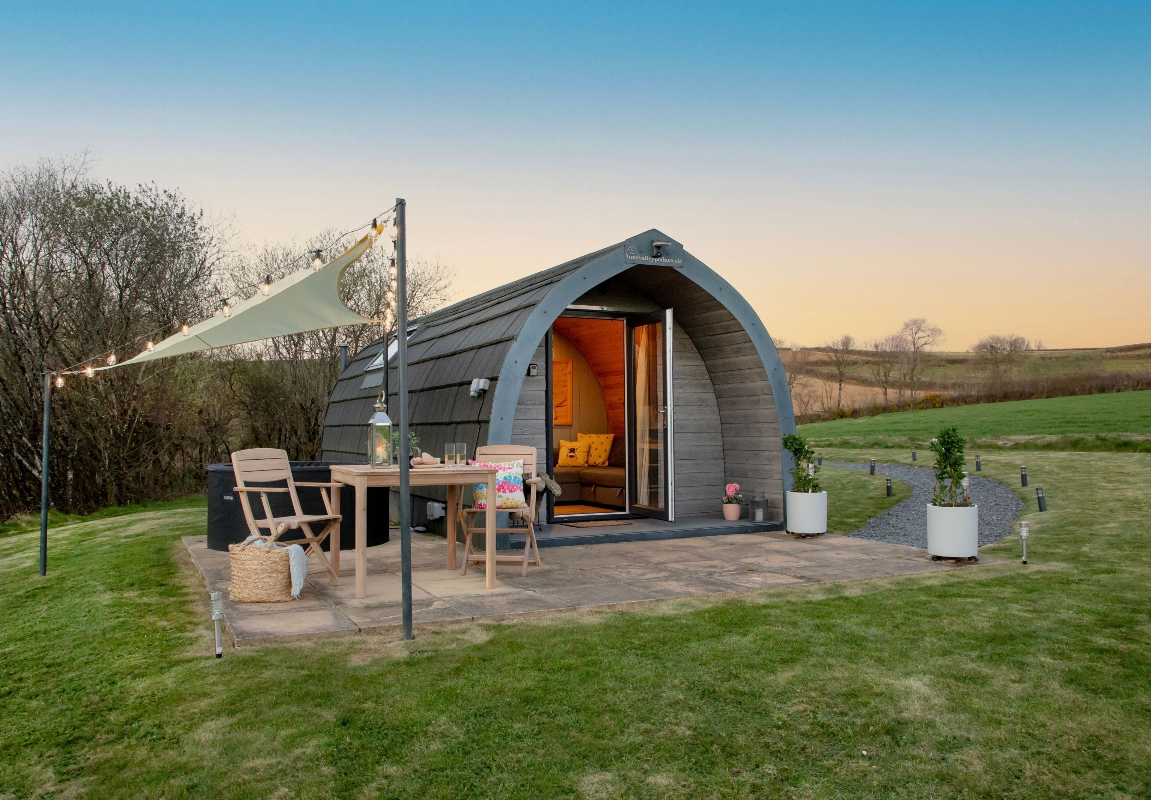 A cozy outdoor pod with a table and chairs, surrounded by a grassy area and trees.