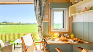 Een eetgedeelte met een ontbijt gedekte tafel, een raam met uitzicht op een groen veld en rieten stoelen.