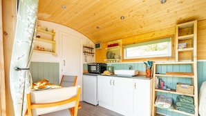 Een kleine keuken met houten kastjes, een magnetron, een spoelbak en een raam boven de aanrecht.
