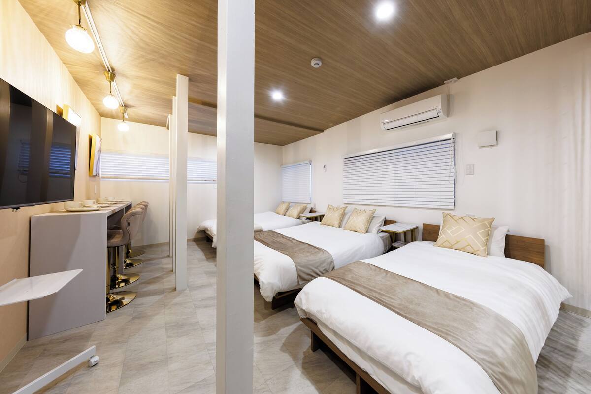A hotel room with two beds, a desk with chairs, a flat-screen TV, and a ceiling with recessed lighting.