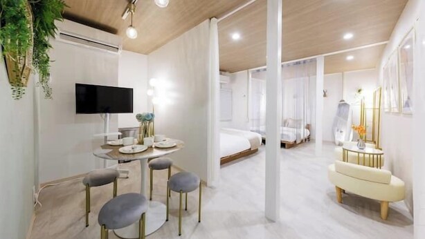 Ein modernes Hotelzimmer mit Flachbildfernseher, einem Essbereich mit rundem Tisch und vier Stühlen, einem Bett mit weißer Bettwäsche sowie einer kleinen Sitzecke mit Bank und Beistelltisch.