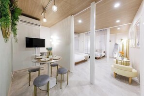 A modern hotel room with a flat-screen TV, a dining area with a round table and four chairs, a bed with white bedding, and a small seating area with a bench and a side table. - Namba Kuromon Central Self Inn (Osaka)