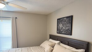 Un lit bien fait, avec une tête de lit, un ventilateur de plafond et une carte de Paris accrochée au mur.