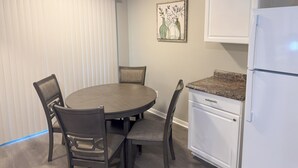 Un coin repas avec une table ronde et quatre chaises, un réfrigérateur blanc et un tableau accroché au mur.