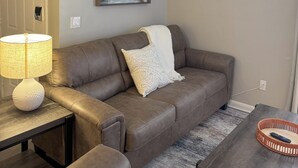 Un salon avec un canapé en cuir marron, un coussin blanc, une lampe et un tableau représentant une vue de la ville, accroché au mur.