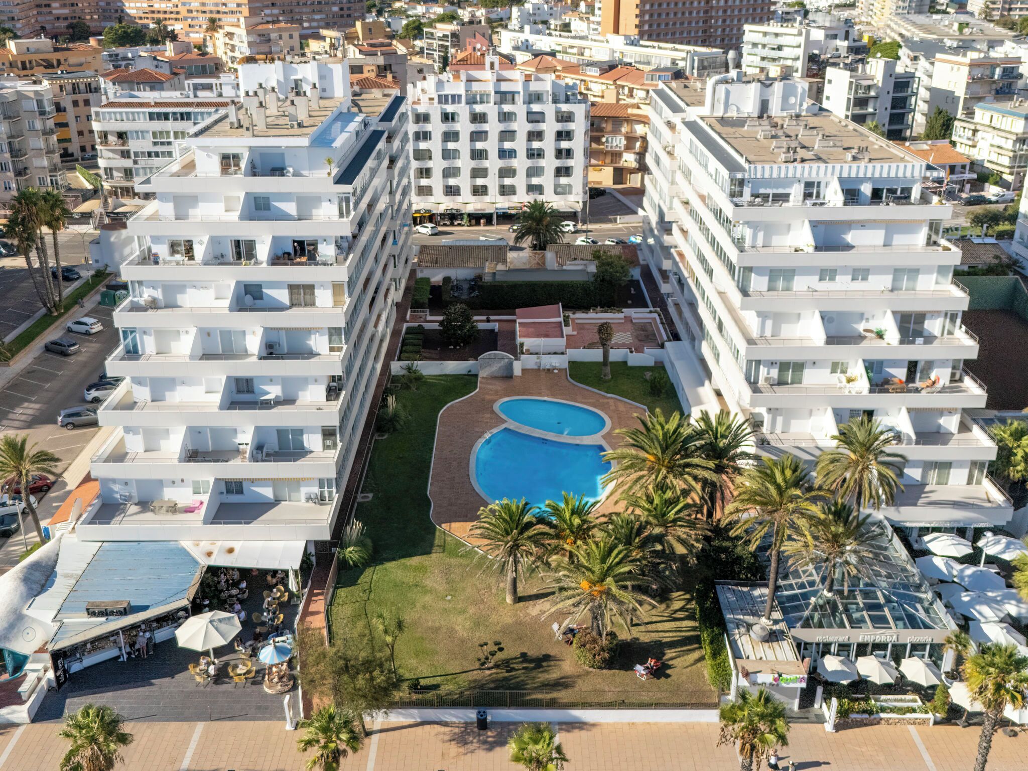 Un hotel moderno de gran altura con varios balcones, una piscina central y palmeras alrededor.