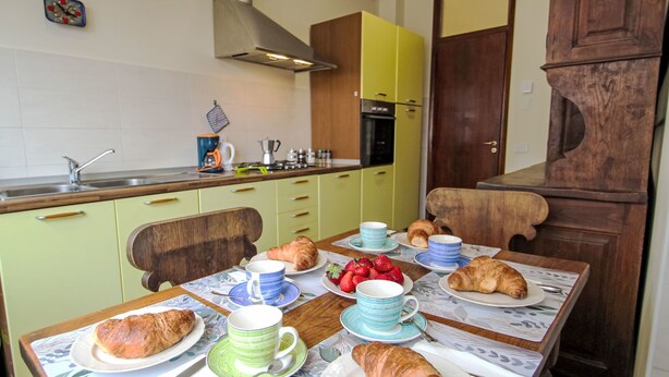 A dining table set with plates of croissants and strawberries, a coffee maker, and a clock on the wall. - Camelia by Interhome (Verbania)