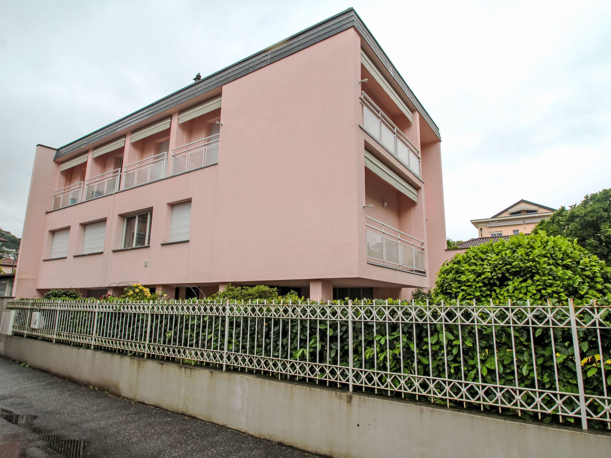 A pink multi-story building with balconies, a gated fence, and greenery.