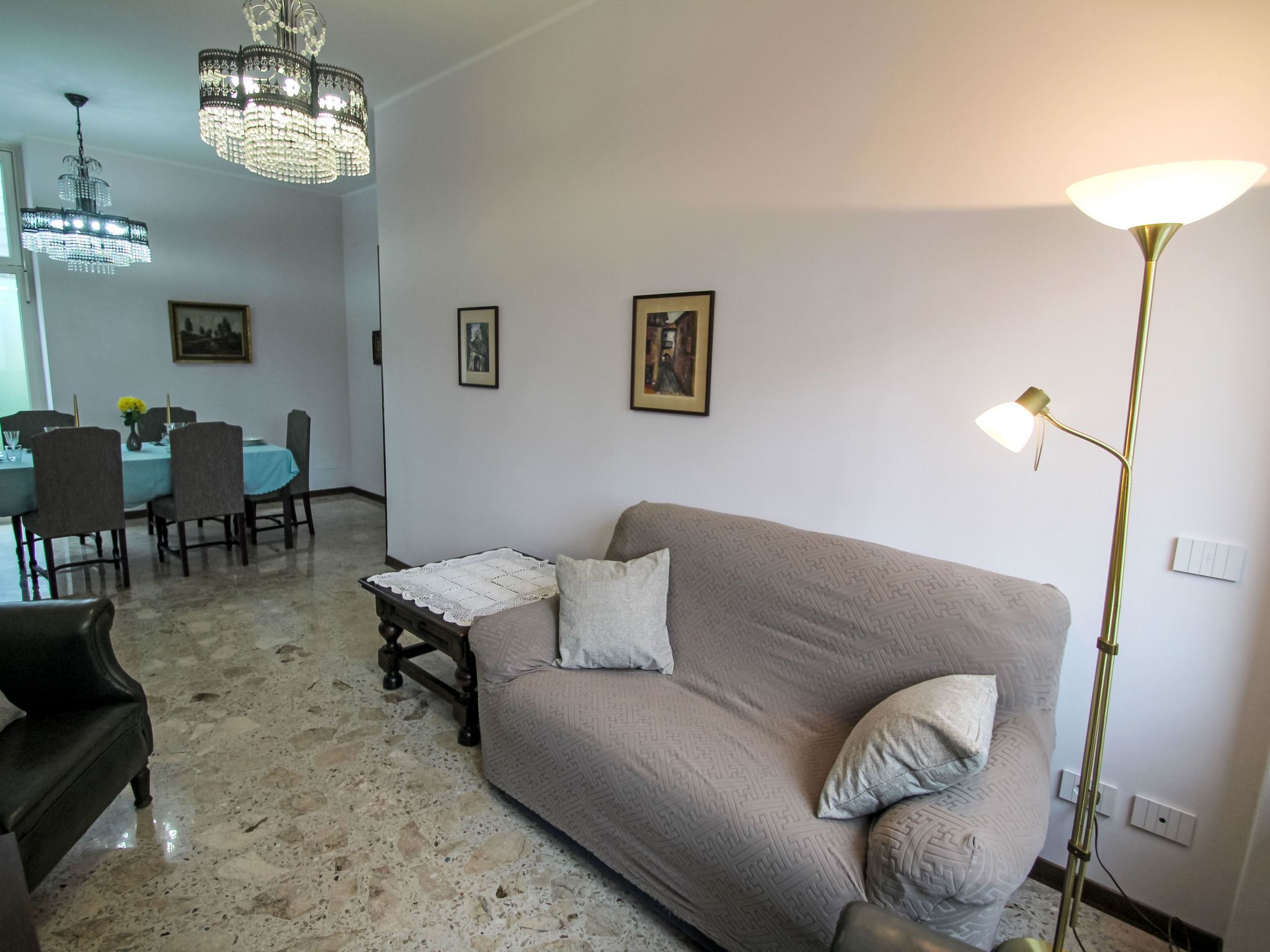 Una sala de estar con un sofá color beige, una mesa de centro, una mesa de comedor con sillas y una araña.