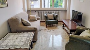 A living room with a sofa, armchair, and a table with a television. - Camelia by Interhome (Verbania)