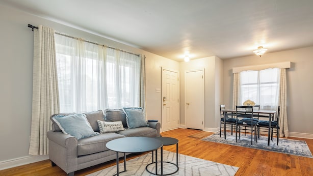 A living room with a grey sofa, two round tables, a dining table with chairs, and a rug.
