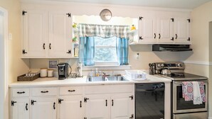 A kitchen with white cabinets, a dishwasher, an oven, and a window with blue curtains.