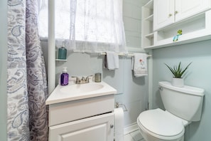 A bathroom with a white sink, a toilet, a shower curtain, and a shelf with toiletries.