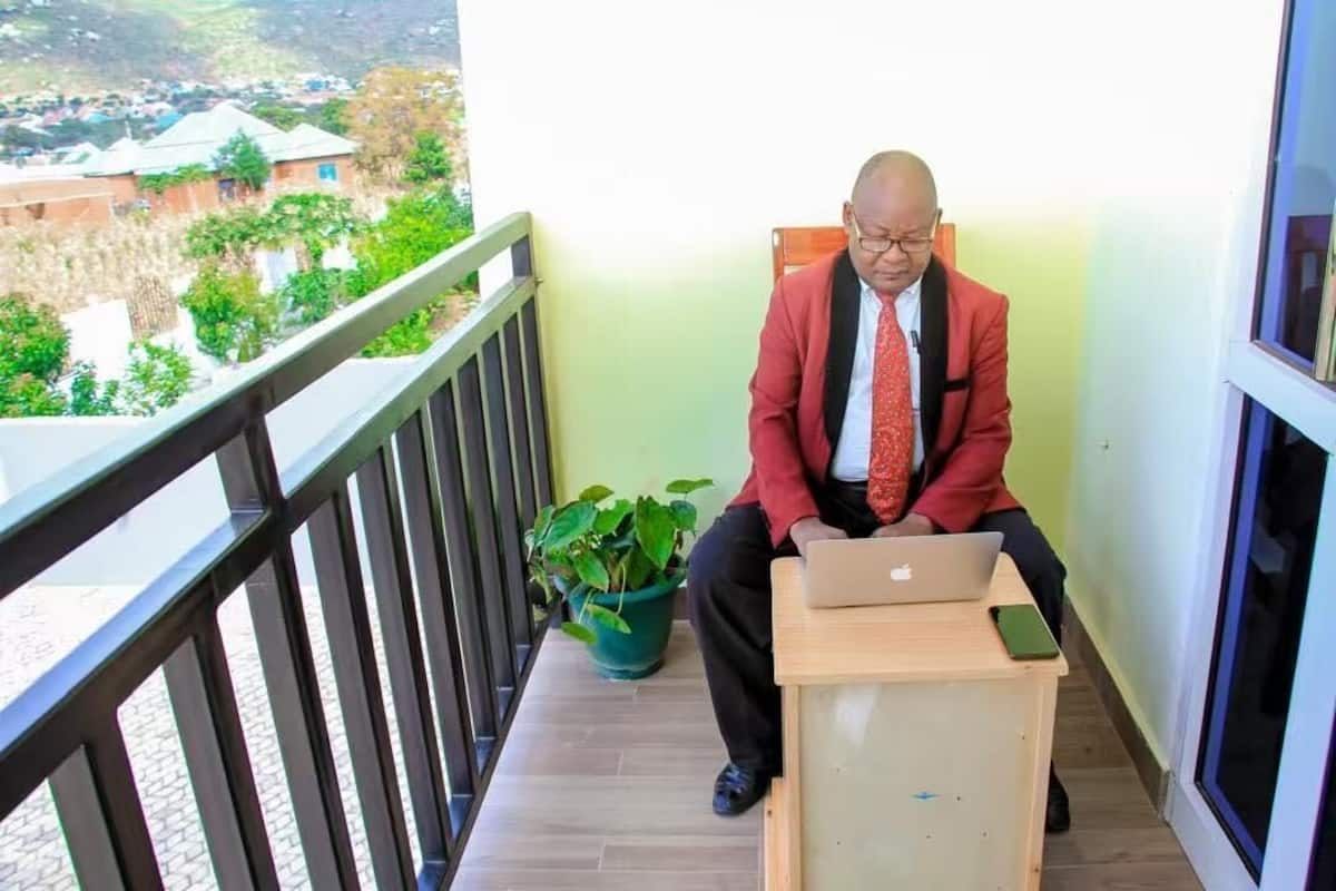 Ein Mann sitzt auf einem Balkon mit einem Laptop, einem Smartphone und einem Blumentopf.