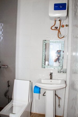 A bathroom with a toilet, sink, and a mirror. - Wooden Haven Hotel (Iringa)
