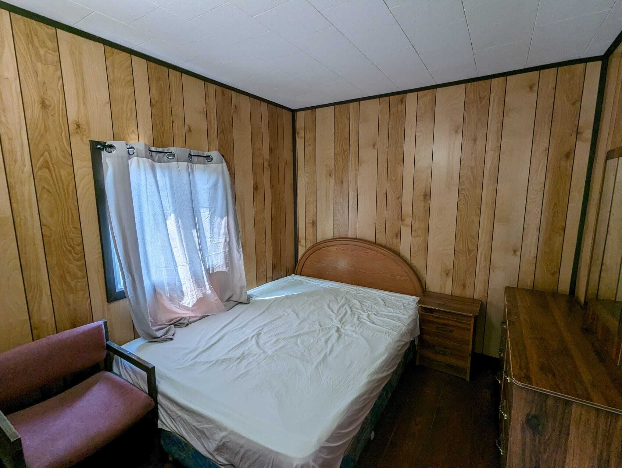 A single bed with a wooden headboard, a small bedside table, a chair, and a wooden wardrobe.