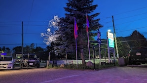 A paved parking area with a fence, a sign for 'Kora Cottages', and a vehicle.