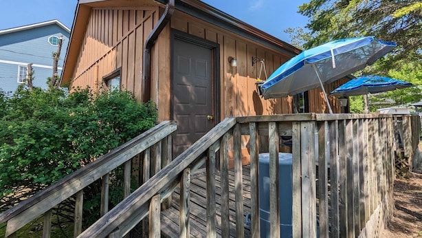 A wooden cabin with a front door, a wooden staircase, and a blue umbrella.
