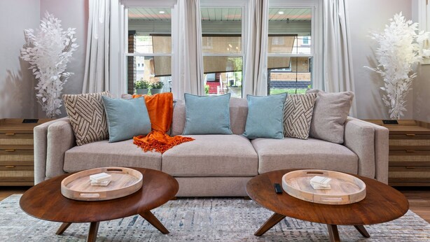A living room with a sofa, two wooden side tables, and a large window with curtains. - Spacious Pittsburgh Home with Deck and Grill (Pittsburgh)