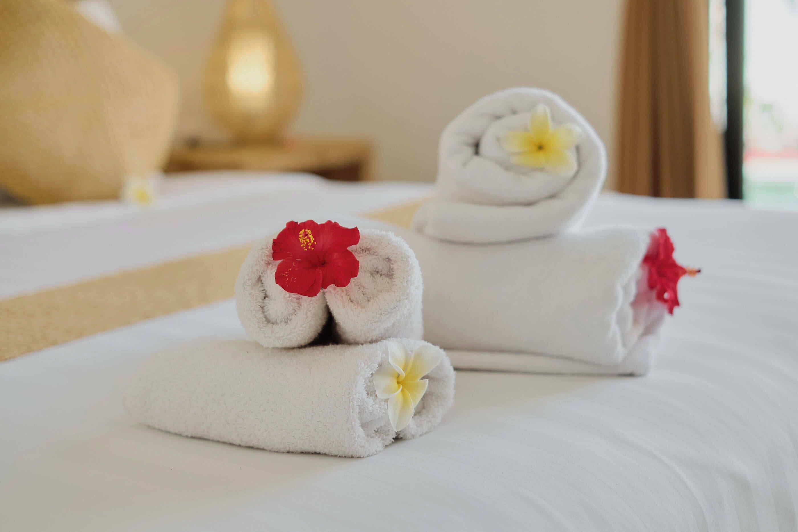 Una cama bien tendida con sábanas y toallas blancas enrolladas adornadas con flores.