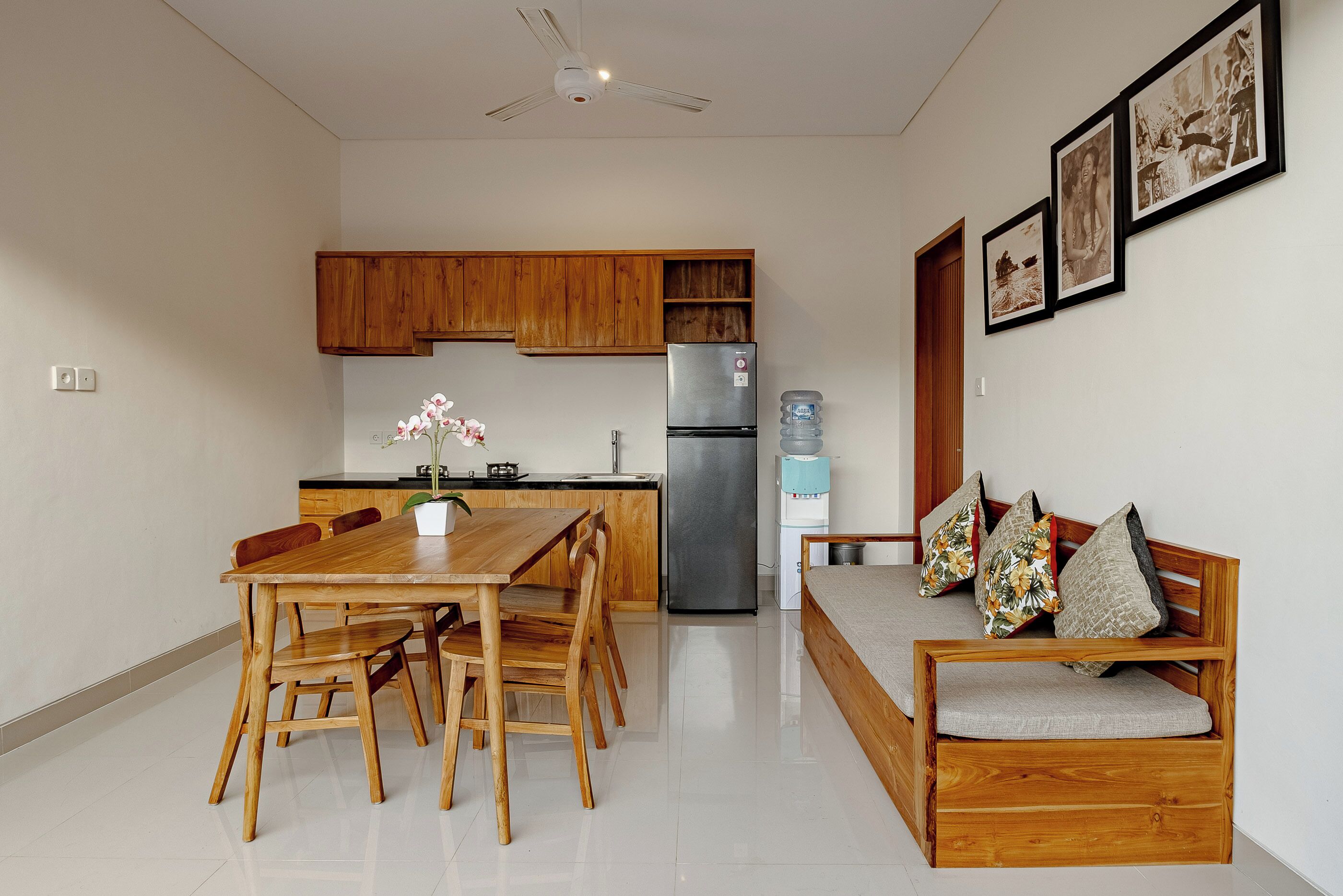 A modern kitchen with wooden cabinets, a stainless steel refrigerator, a dining table with chairs, and a bench with cushions.
