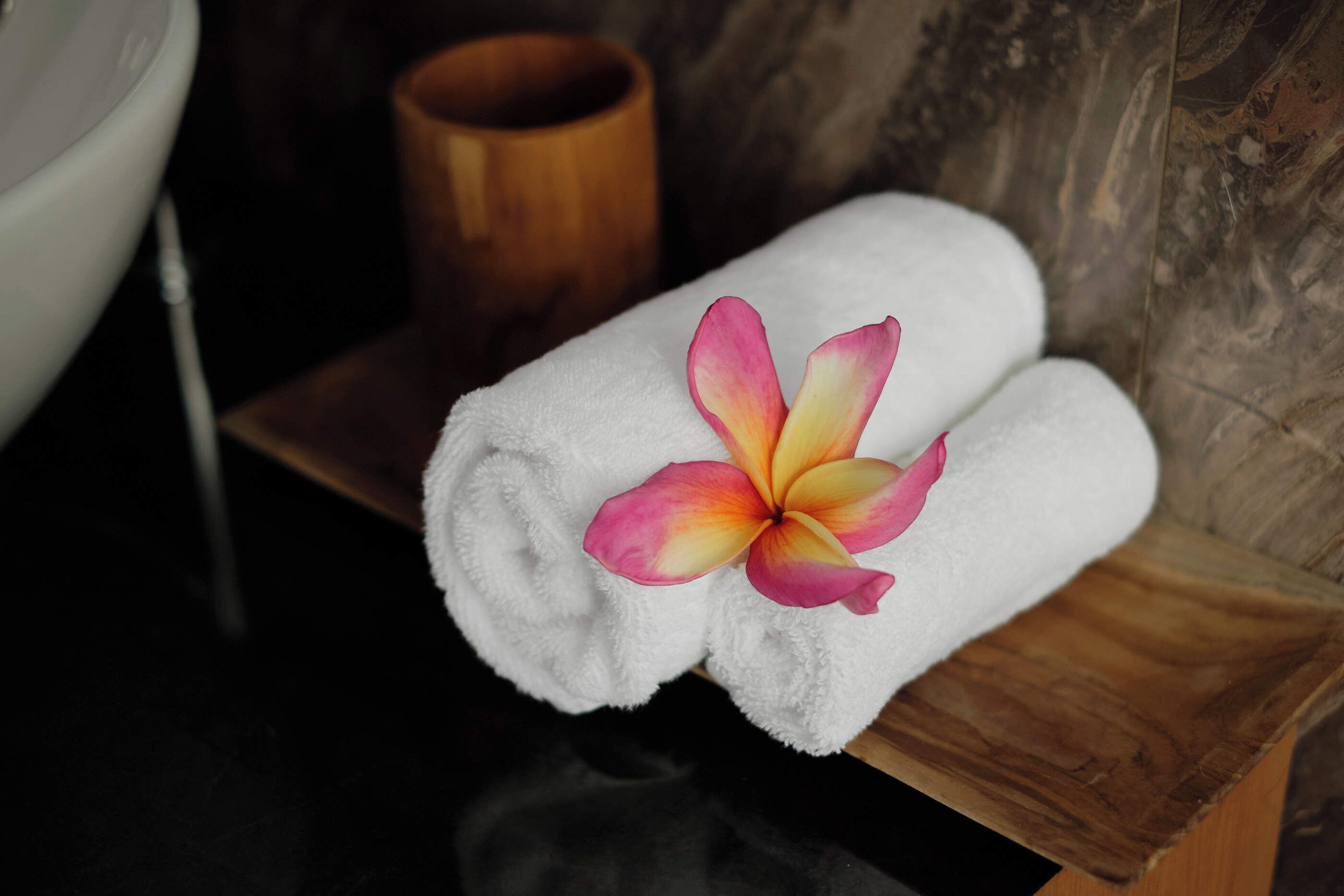 A white towel with a pink and yellow flower on a wooden bench in a bathroom.