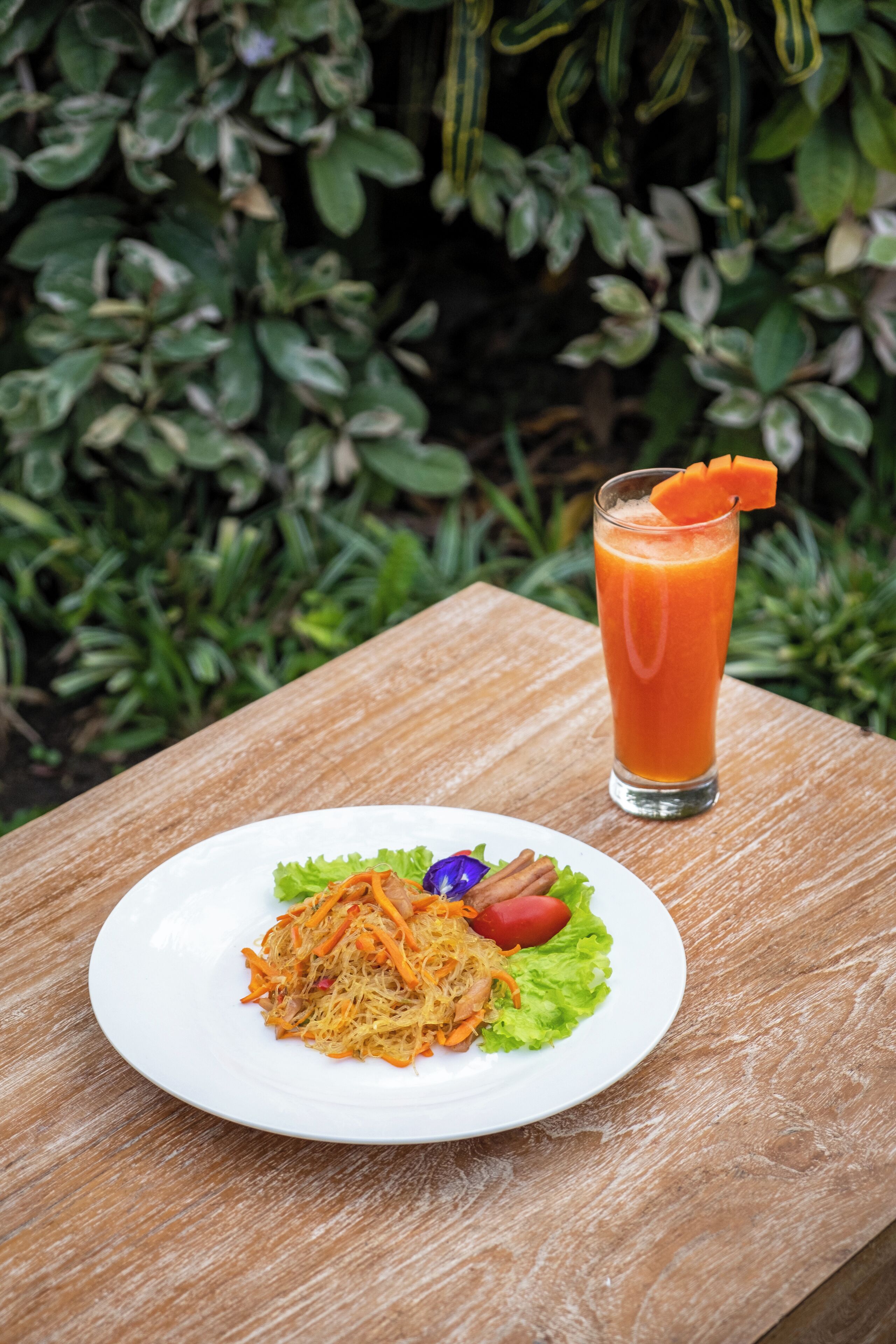 A white plate with a salad and a glass of orange juice on a wooden table.