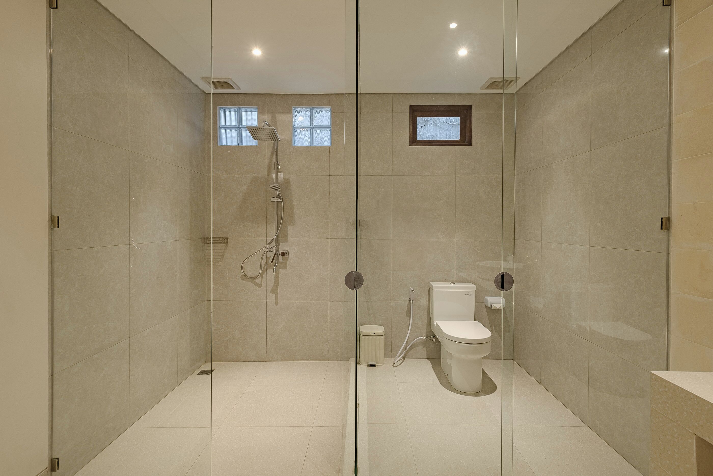 A modern bathroom with a glass shower enclosure, a toilet, and a small window.