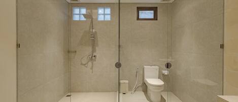 A modern bathroom with a glass shower enclosure, a toilet, and a small window.