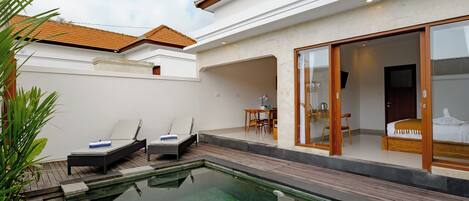 Uma área de piscina moderna com espreguiçadeiras, um deck de madeira e um quarto com paredes de vidro.