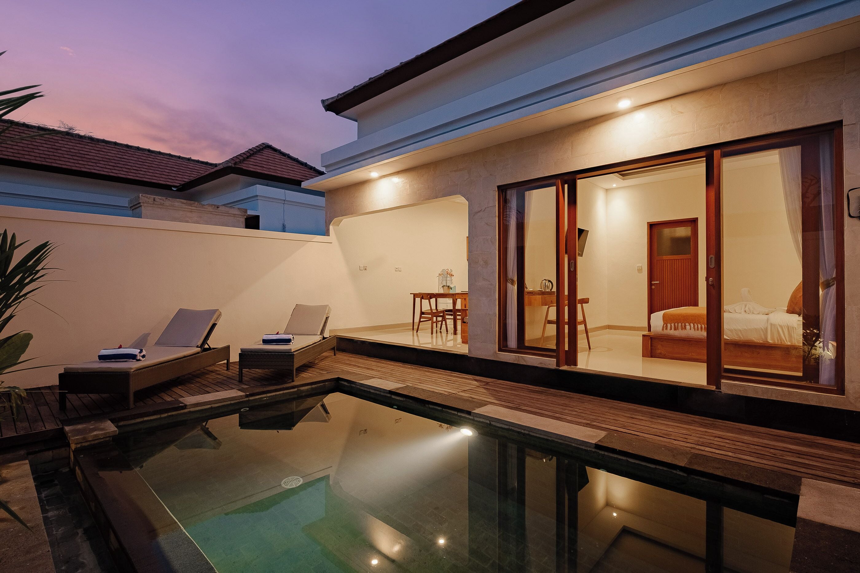 Una casa moderna con piscina, zona de comedor y un dormitorio visibles a través de amplios ventanales correderas.